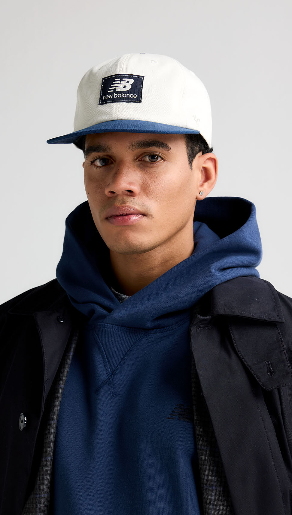 A close-up portrait shot of a man wearing a white &lsquo;47 hat that has the New Balance logo on the front center of the hat with a blue cap.    