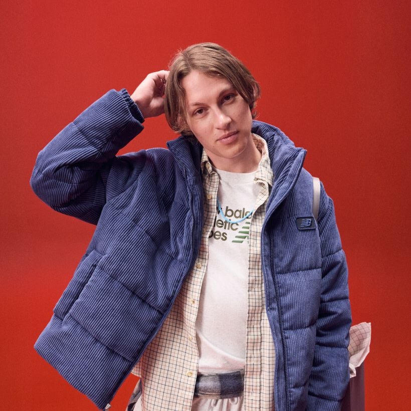 Man in a blue jacket scratching his head on a red background.