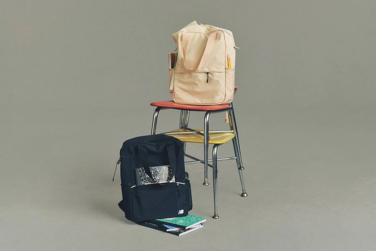 Studio image of a cream colored and a navy colored New Balance backpack placed on a metal chair.