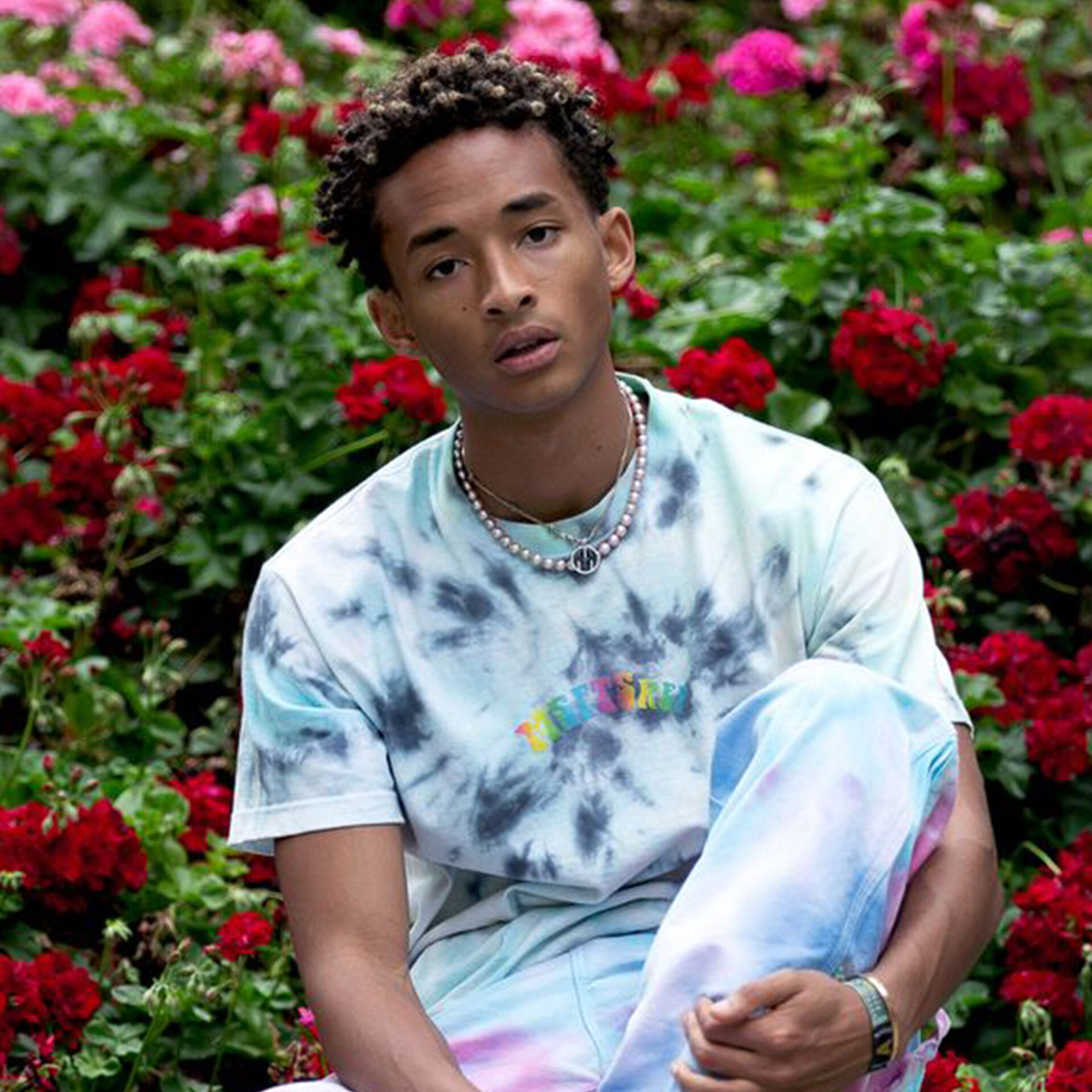 Jaden Smith en tenue de soirée, assis devant des fleurs.