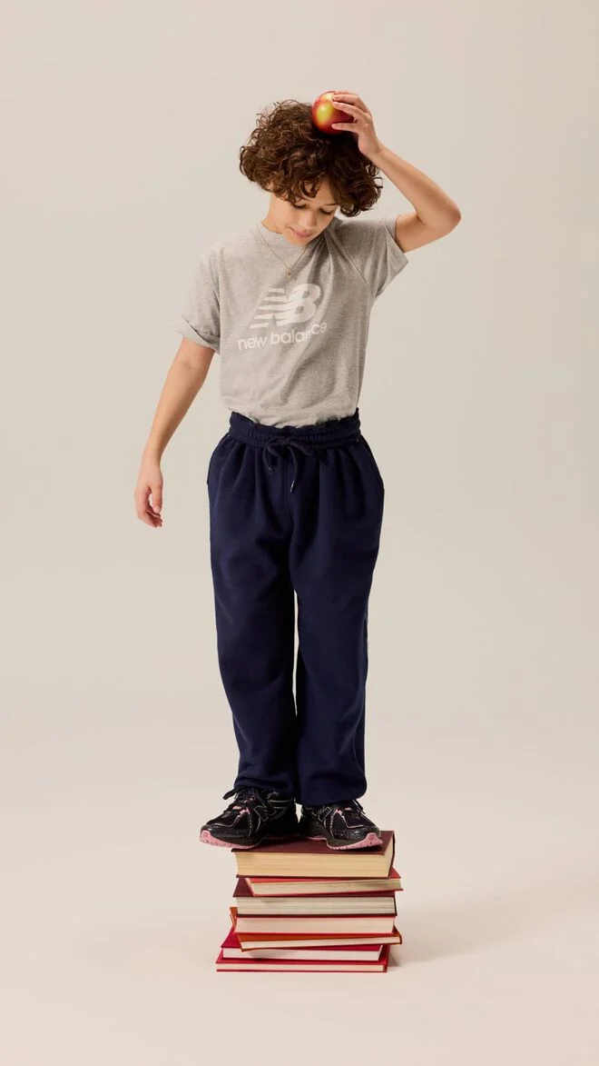 Kid standing on a pile of books while holding an apple on his head. 