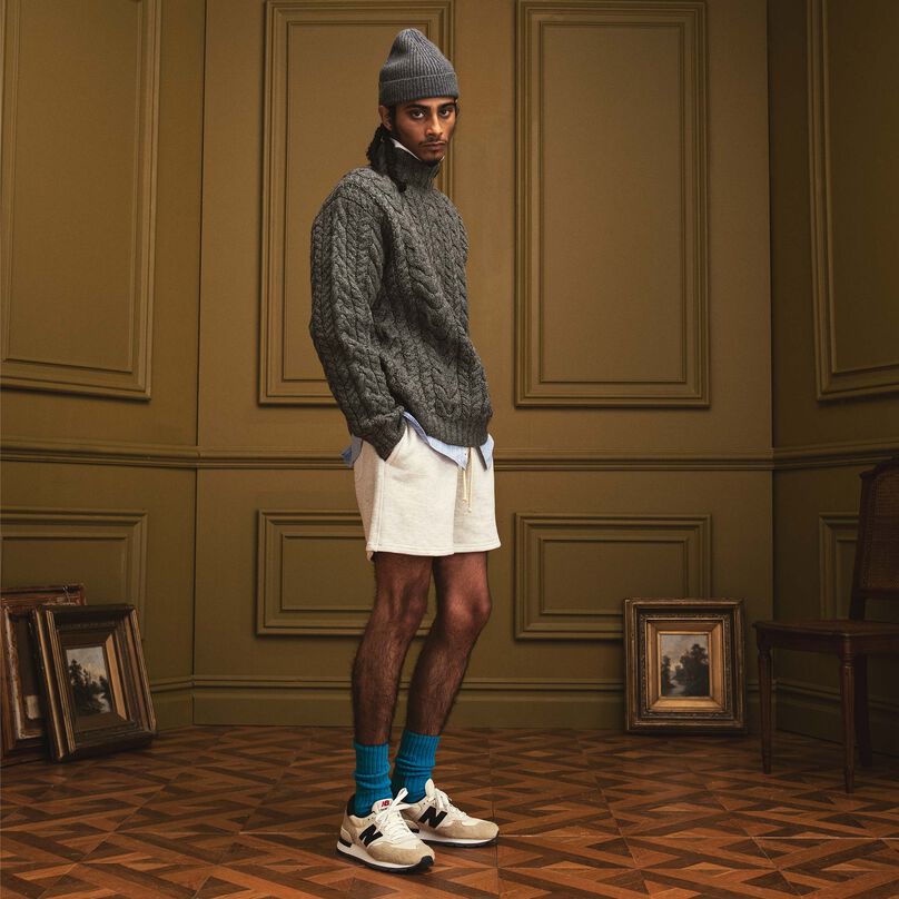 A man wearing MADE in USA apparel and the cream 990v1 standing in a beautiful indoor environment with his hands in his shorts.