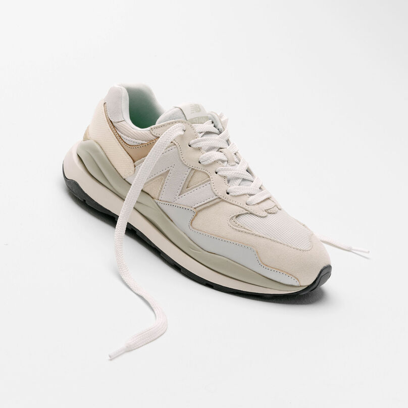 An off-white and grey 57/40 sneaker sitting in a grey studio environment with its laces pulled out.