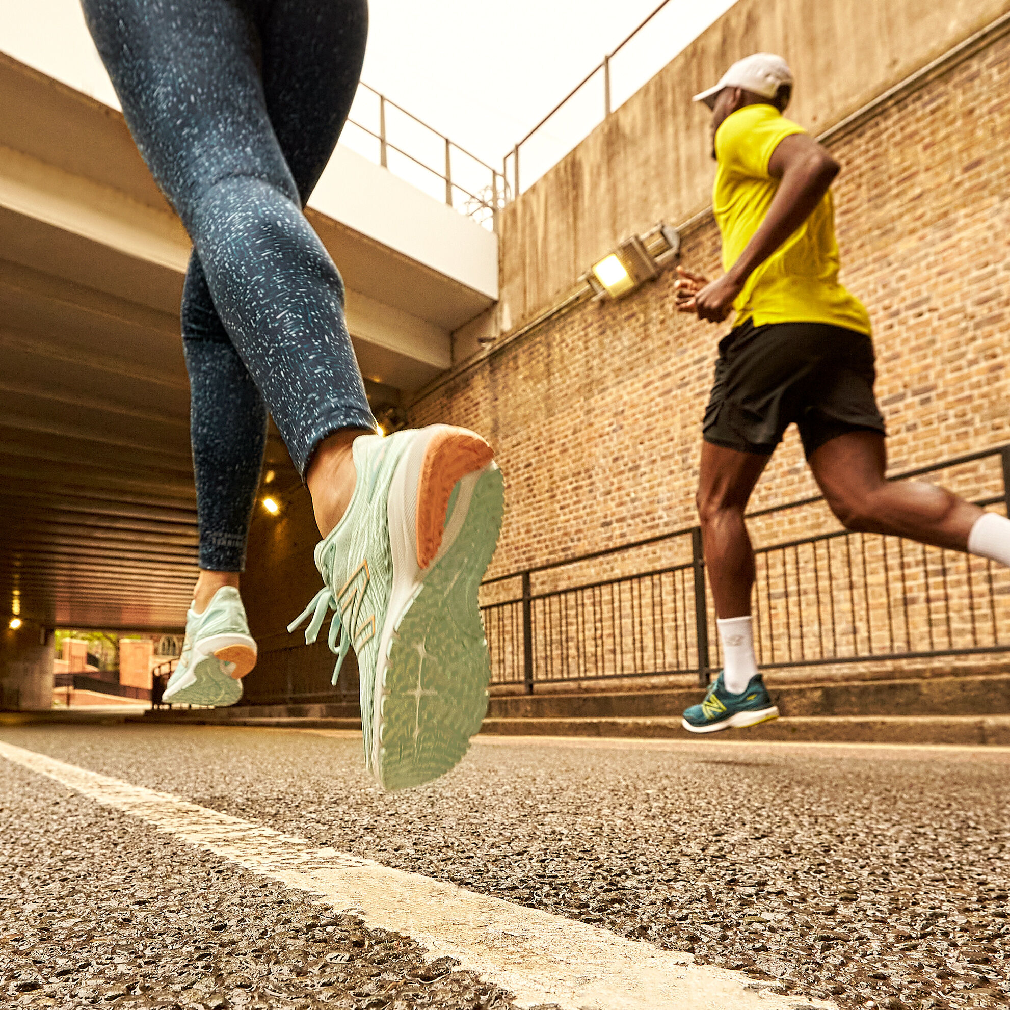 Vue à partir des genoux d'un coureur et d'une coureuse, qui porte un legging aux motifs bleus et des chaussures Fresh Foam X 860v12 de couleur bleue claire, tandis que le coureur est vêtu d'un t-shirt jaune, d'un short noir et de chaussures Fresh Foam X 860v12 de couleur verte foncée
