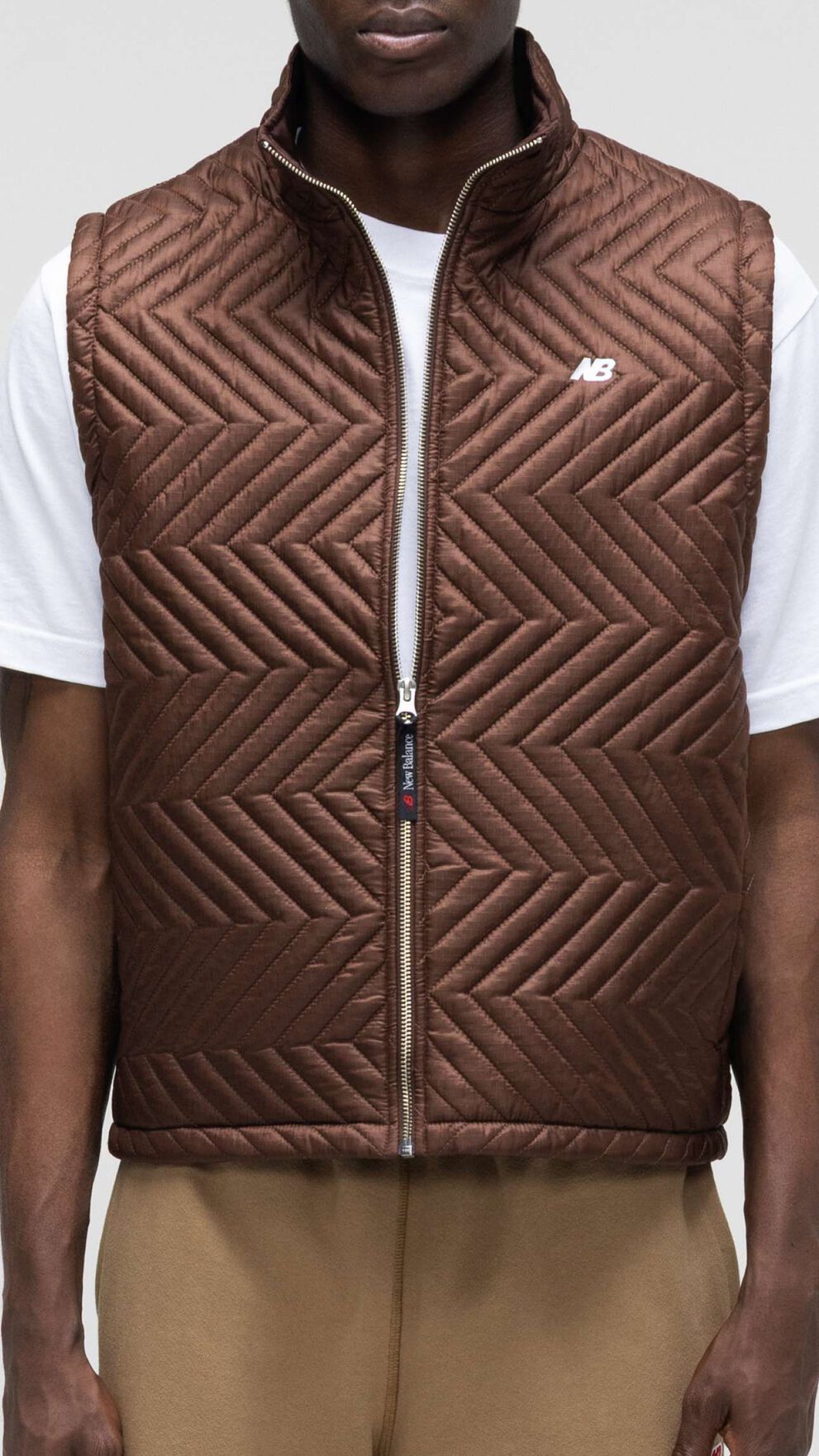 Une personne v&ecirc;tue d'un cardigan marron, debout devant un fond de studio gris