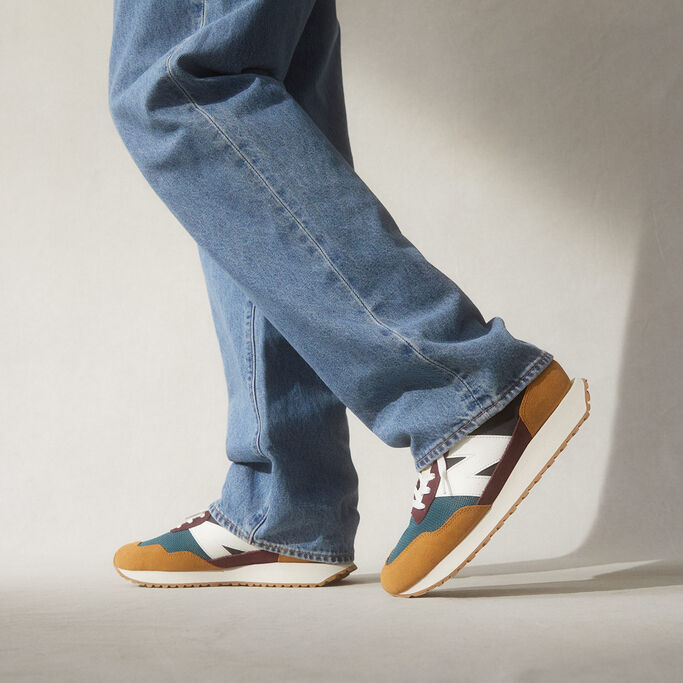 Man wearing burgundy, blue and tan 237 shoes with jeans, cropped at the knee