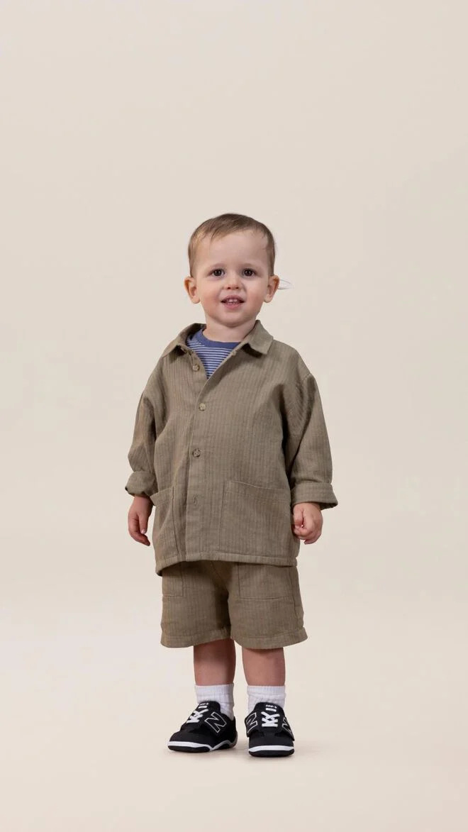 Toddler wearing an army green matching set standing in front of a beige background. 