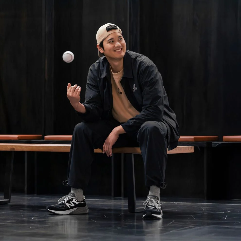 Ohtani assis dans un vestiaire lançant une balle dans les airs.  