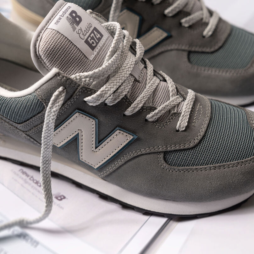 Close up shop of a pair of unlaced grey 574 on a pile of New Balance archival ads.