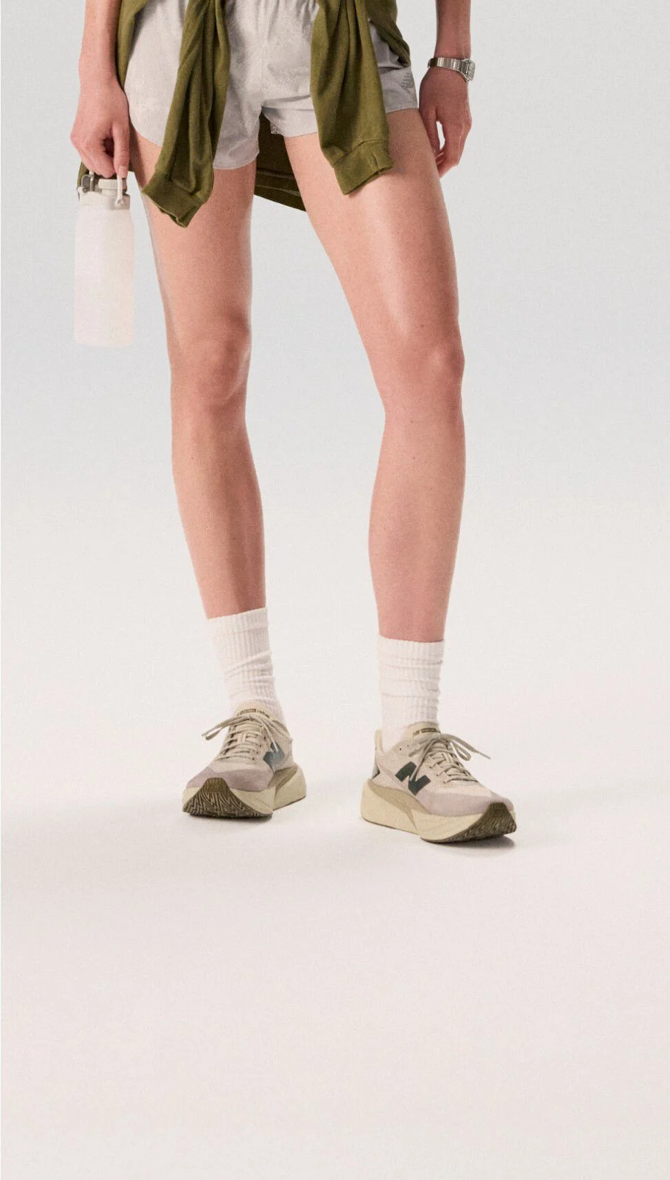 Jeune femme debout sur un fond blanc portant des chaussures de course blanches.