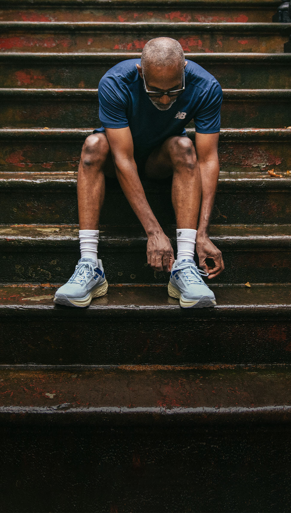 Runner Aaron Ganaway wearing blue 1080v13 shoes sitting outside on the steps of a brownstone.