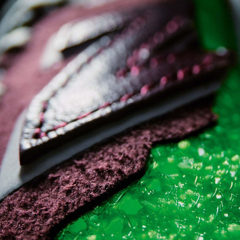 Une photo de détail dramatiquement éclairée des textures supérieures d’une chaussure de course FuelCell RC Elite brun rougeâtre foncé nb Stone Island Tokyo Design Studio avec des accents vert lime