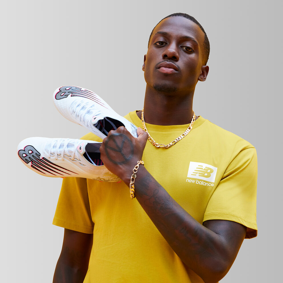 Vêtu d'un t-shirt jaune, Tim leve des chaussures de soccer dans les airs sur un fond gris.