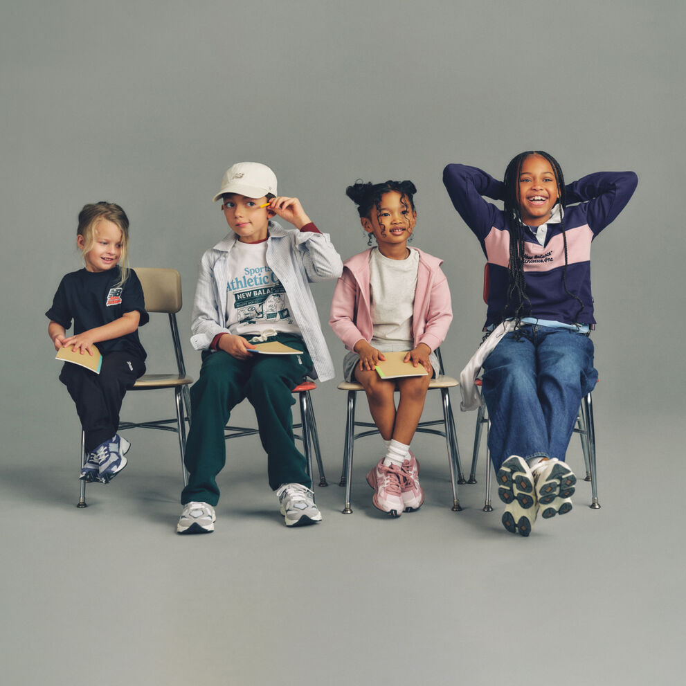 Four kids seated side-by-side on simple wooden chairs against a plain, neutral background, arranged in a horizontal line.