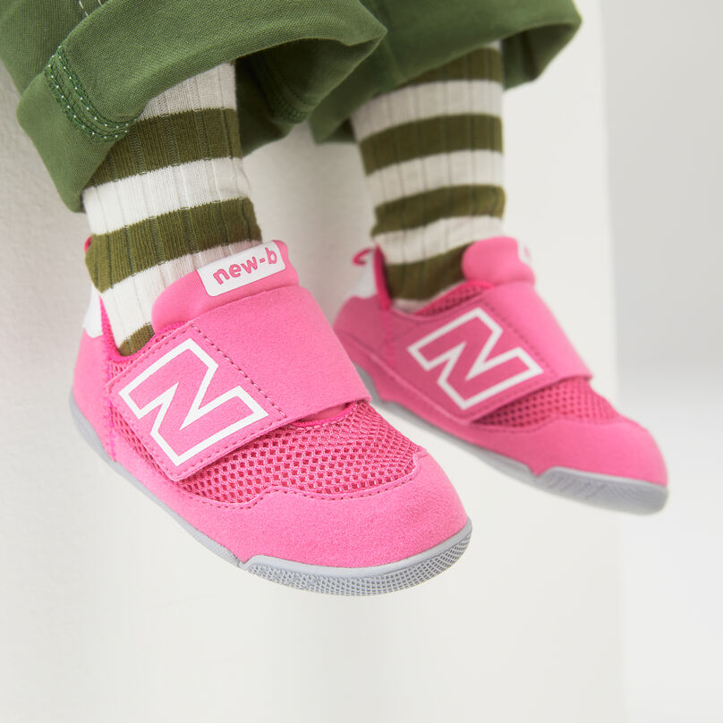 Un enfant portant des chaussettes à bandes vertes et blanches avec de nouvelles chaussures New-B rose les pieds pendants