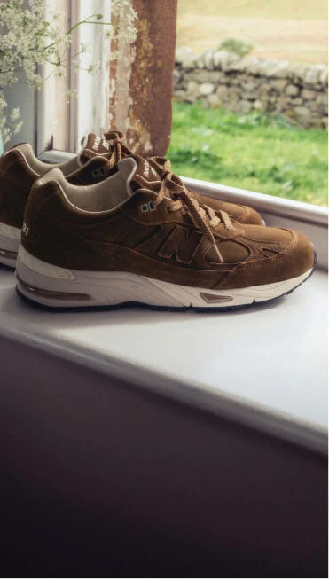 Une paire de baskets New Balance Made in UK sur un rebord de fen&ecirc;tre &agrave; c&ocirc;t&eacute; d'un petit vase de fleurs blanches.