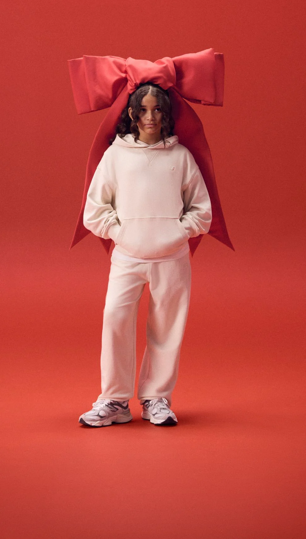 Kid wearing a large red ribbon on her head in a white outfit. 