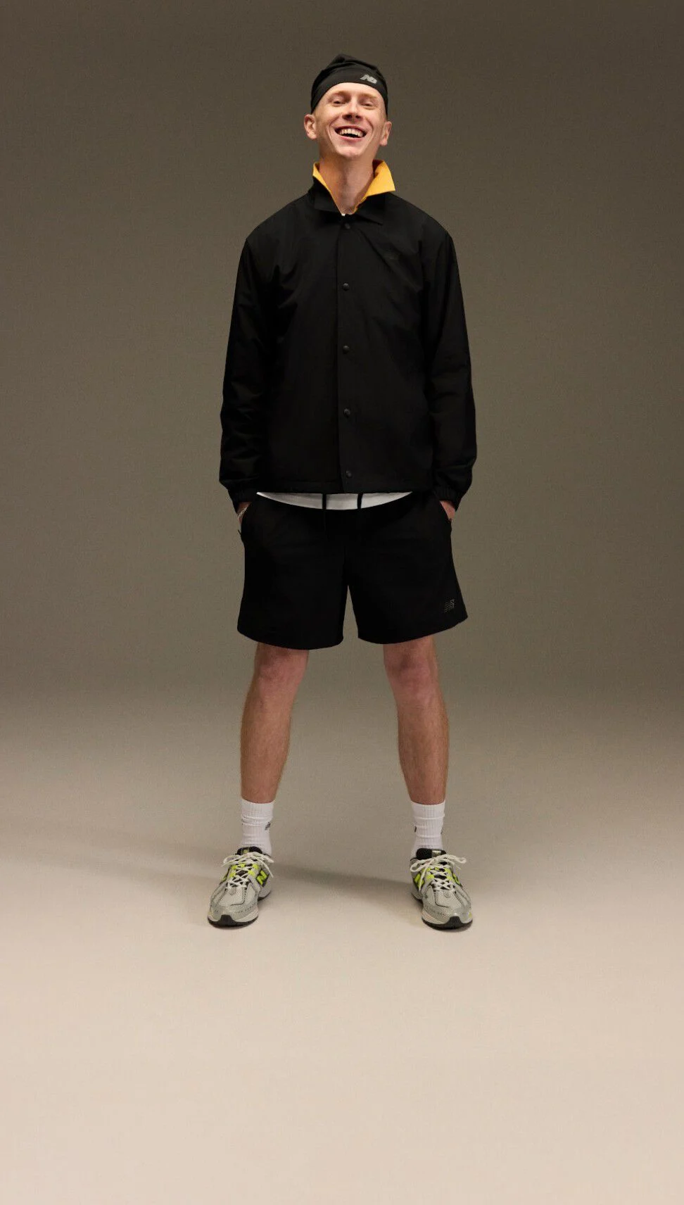 Un homme posant en tenue sportive devant un fond brun et beige.