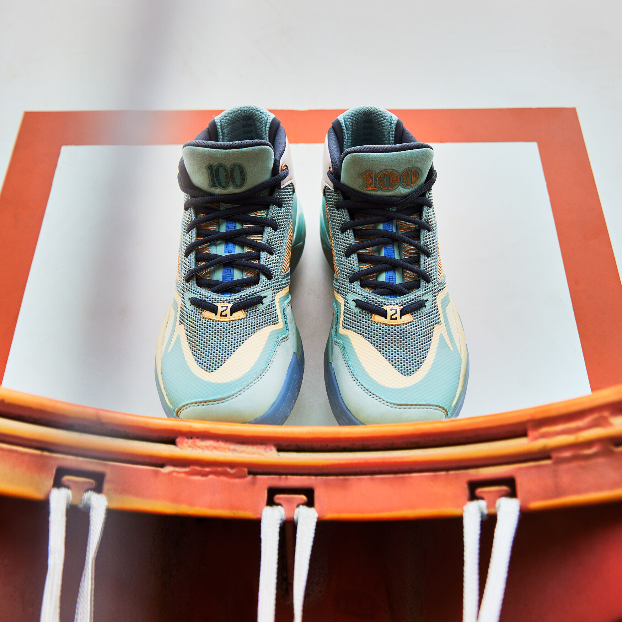A pair of light green KAWHI signature shoes facing forward on a basketball rim, toes touching the rim and soles against the backboard