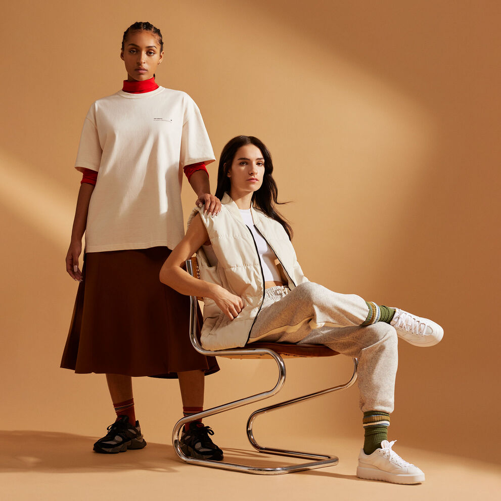 Two women wearing NB Uni-ssentials clothing posing in front of a burnt orange studio backdrop 