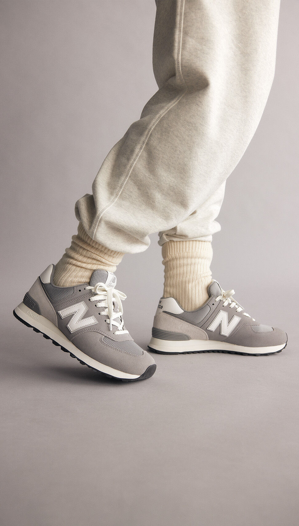 Photo d’un personne agenouillée portant des baskets grises NB 574 avec un pantalon de sport léger et des chaussettes hautes
