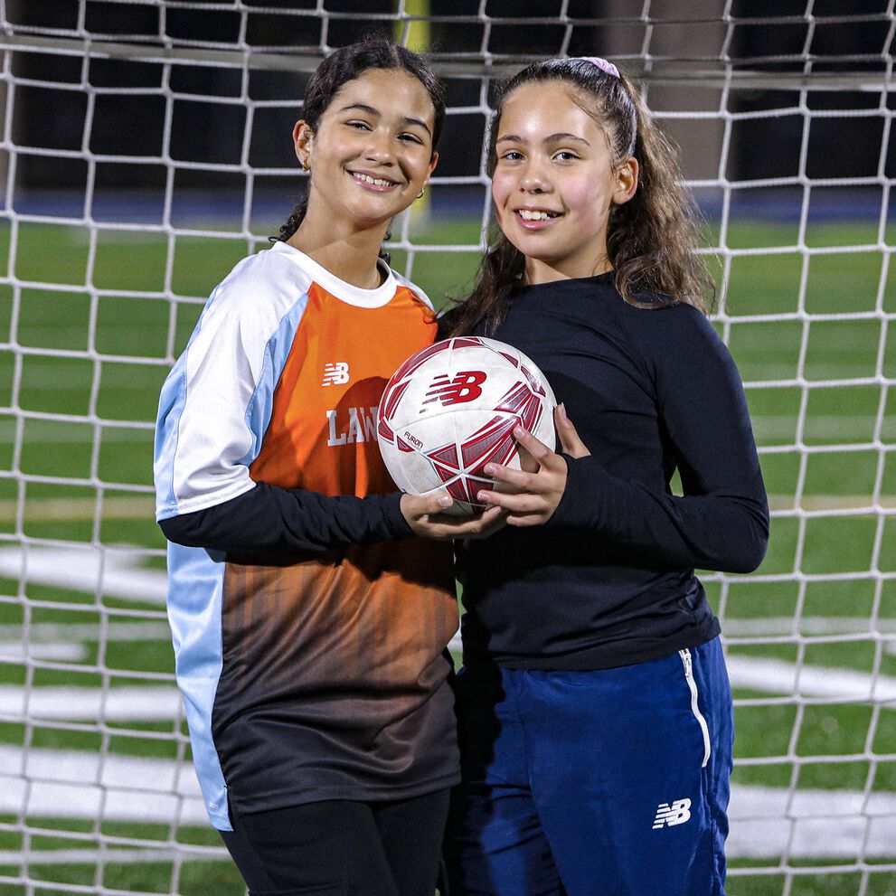 Deux adolescentes souriantes posant avec un ballon de football devant un but.