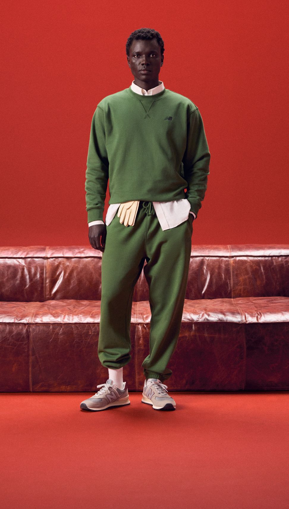 Young man in a green outfit standing in front of a red couch. 