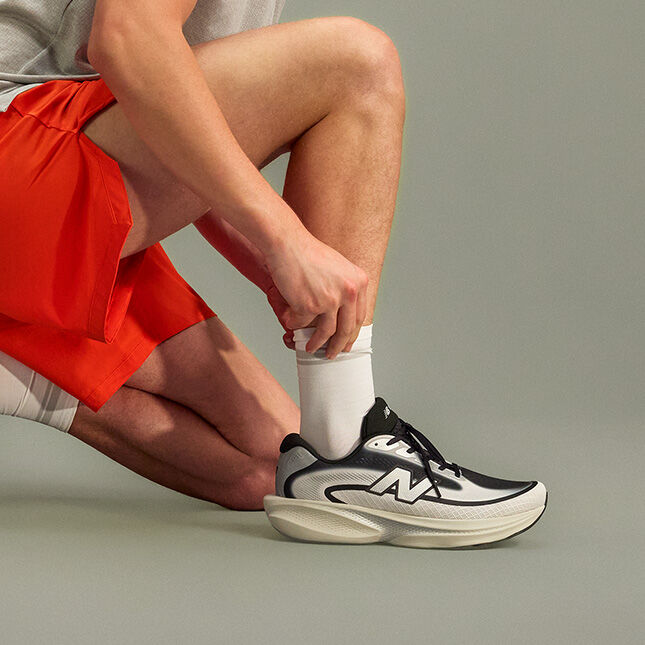 Close-up studio image of a person kneeling on one knee against a smooth, neutral gray background.