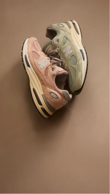 Top down view of two New Balance Made in UK sneakers resting against one another in a beige studio environment. 