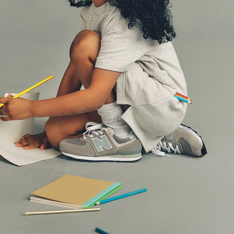 Gros plan pris en studio d'un enfant accroupi sur le sol, devant un fond uni gris clair, concentr&eacute; sur un dessin qu'il r&eacute;alise sur une feuille de papier lign&eacute;. 