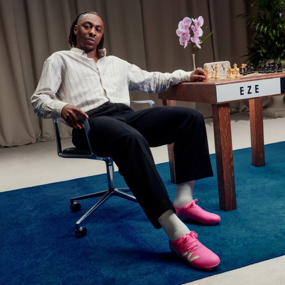 Eberechi Eze sitting in a chair beside a chess table, wearing bright pink New Balance sneakers.