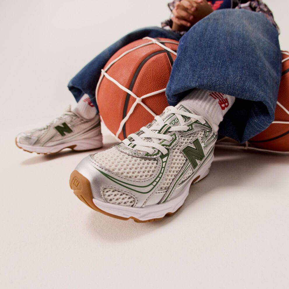 Un enfant portant des chaussures argentées assis sur un filet de ballons de basket. 