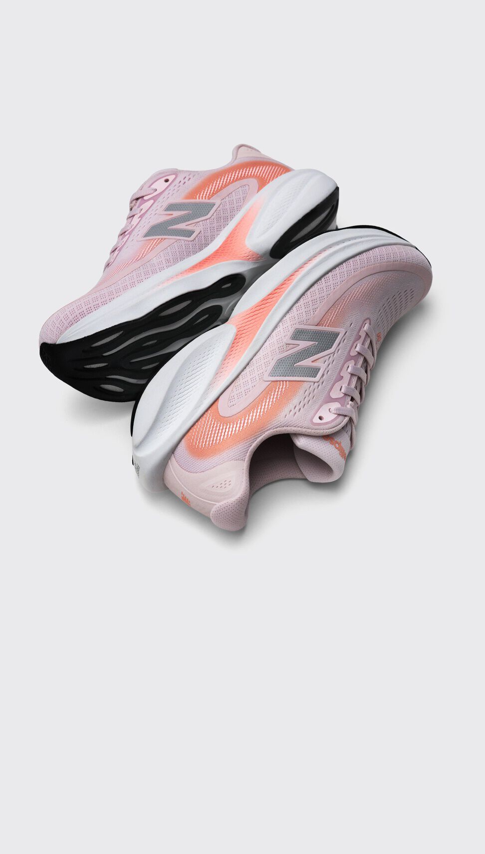 Une paire de chaussures de course New Balance rose p&acirc;le avec des accents corail et des semelles &eacute;paisses noires et blanches affich&eacute;es sur un fond gris clair.