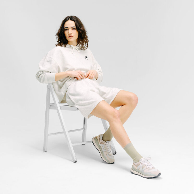 Woman sitting in a chair wearing off-white NB apparel and the Grey Day 57/40 sneakers in a grey studio backdrop.