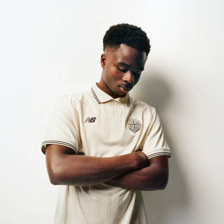 Saka looking down with his arms folded wearing a beige jersey.