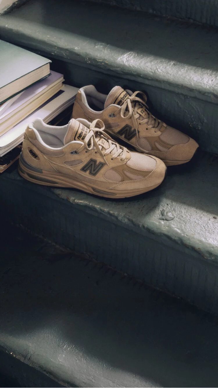 Une paire de chaussures sport New&nbsp;Balance Made in UK sur un escalier, &agrave; c&ocirc;t&eacute; d&rsquo;une pile de livres.