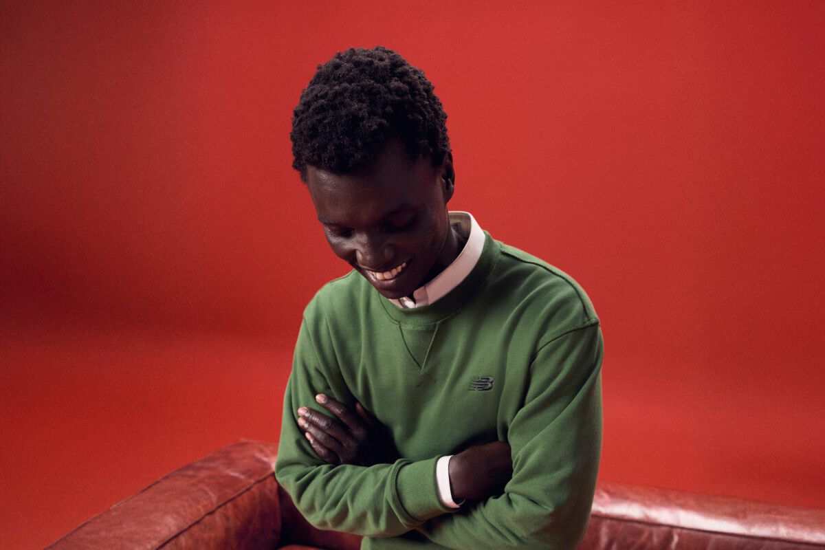 Un homme vêtu d’une tenue verte qui riait devant un canapé rouge.