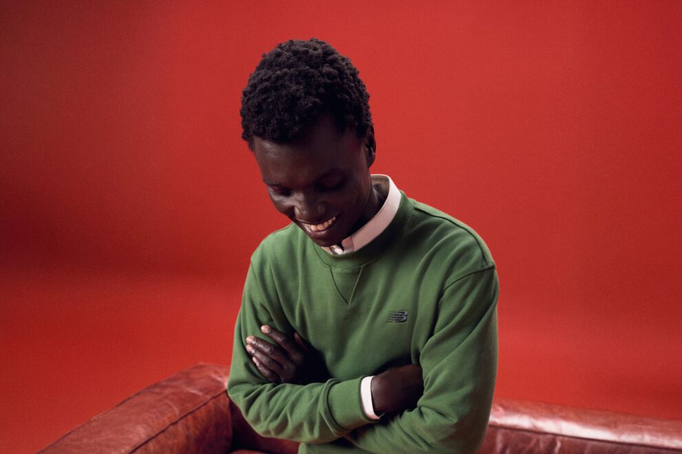 Un homme vêtu d’une tenue verte qui riait devant un canapé rouge.