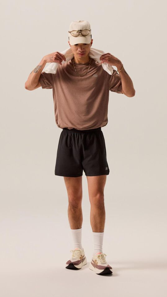 Un homme vêtu d'un short noir et d'une chemise brune, tenant une serviette au-dessus de sa tête. 