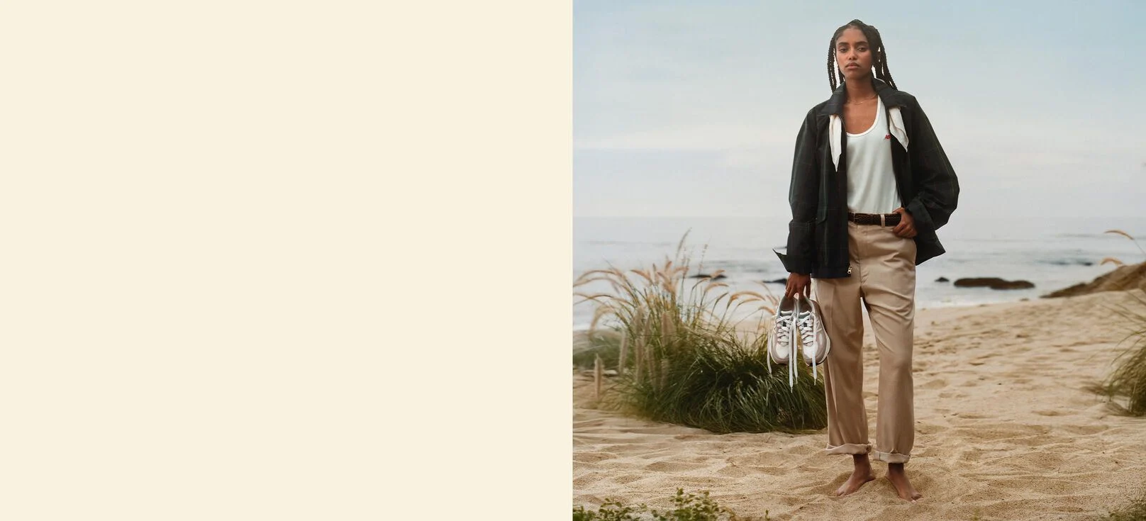 Une femme debout sur une plage, tenant une paire de chaussures 990v6. 