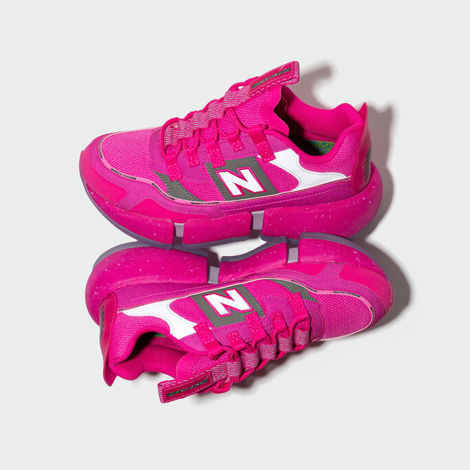 Vue à la hauteur du sol d'une paire de chaussures Vision Racer rose l'une posée contre l'autre sur un fond de studio gris.
