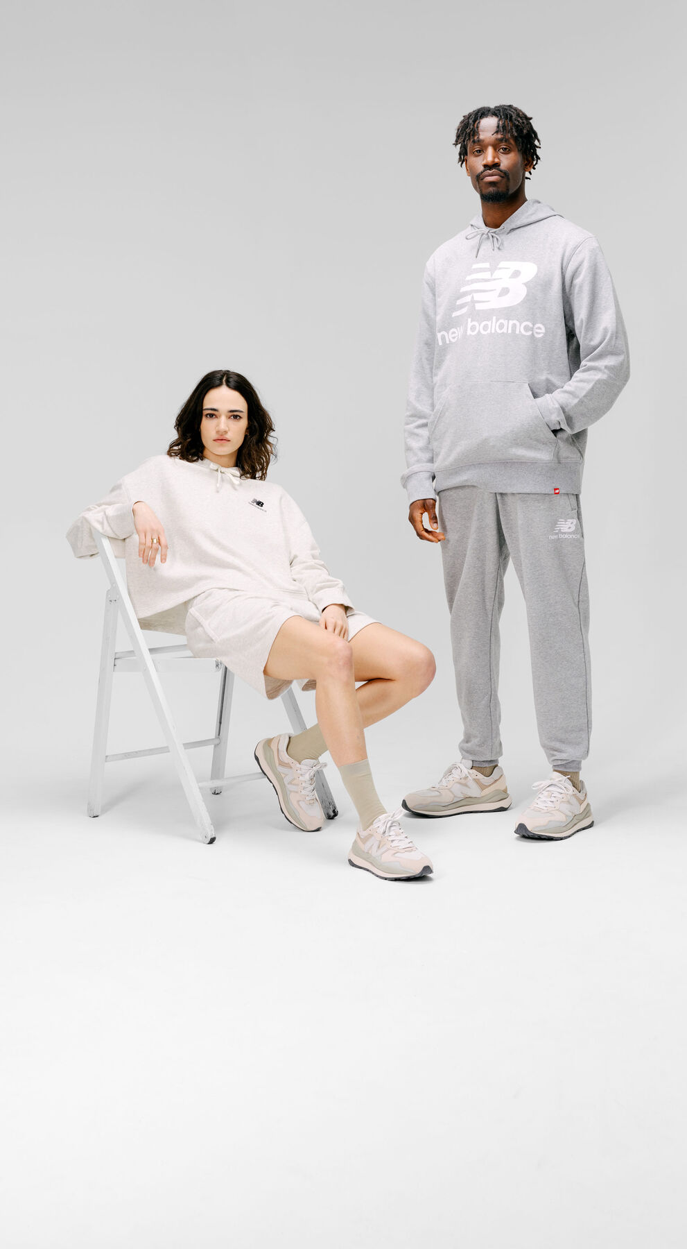 Homme et femme portant des vêtements et des chaussures New Balance gris dans un décor de studio gris. 