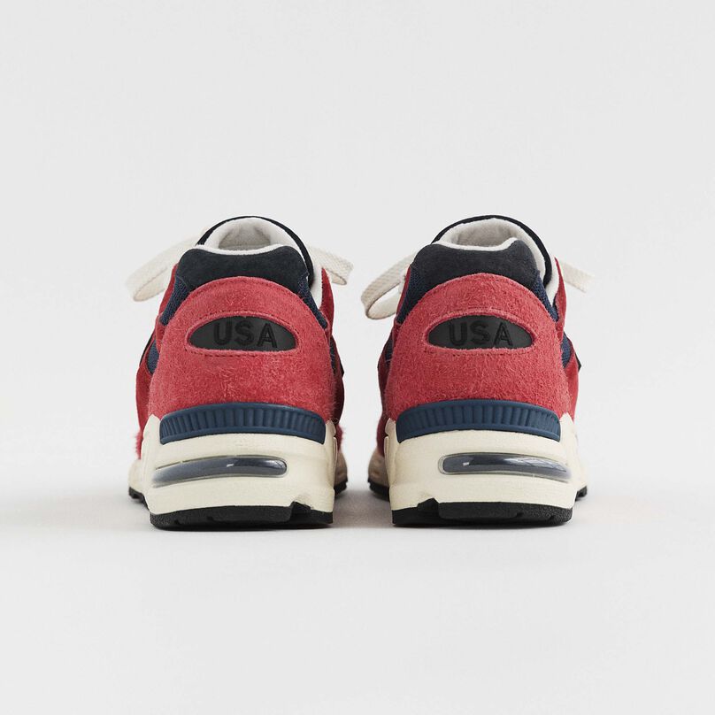 A pair of red and navy 990v2 turned away showing the back heel details.