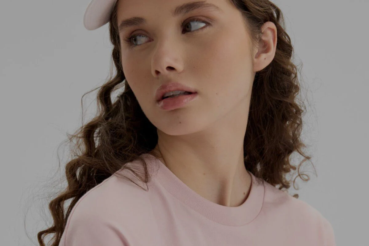 Gros plan d'une femme portant une chemise rose p&acirc;le et un chapeau.