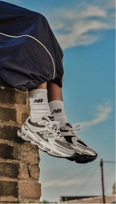 Someone sitting on top of a brick wall with their feet dangling wearing grey and black shoes. 
