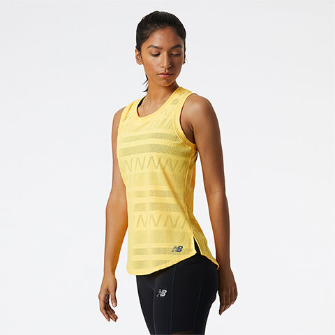 Woman standing in grey studio backdrop wearing yellow sleeveless shirt and black leggings. 