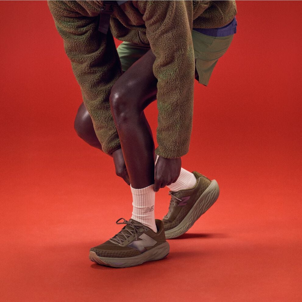 Jeune homme qui se penche pour lacer ses souliers sur un fond rouge.