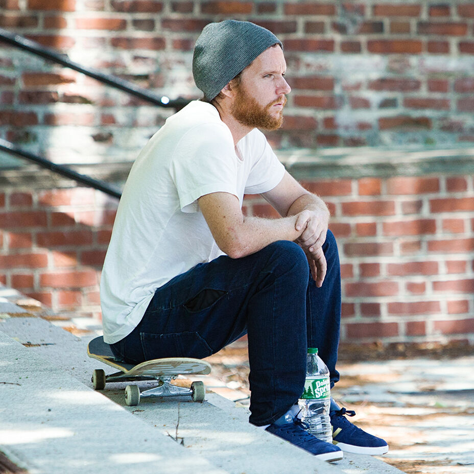 Skateboarder PJ Ladd seated on his board on a concrete staircase