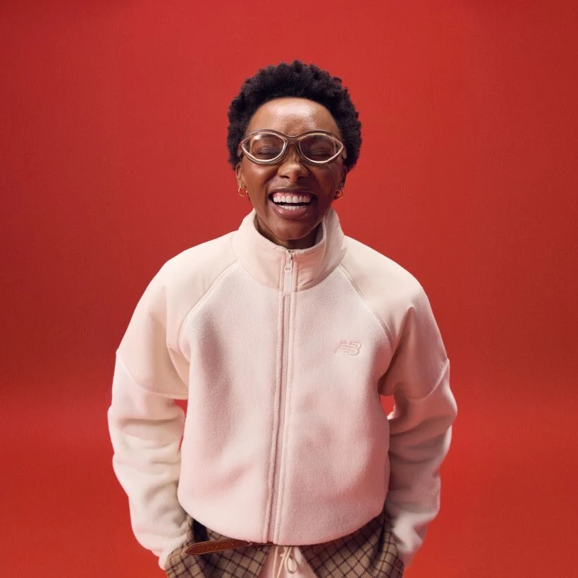 Woman laughing in a white zip-up jacket on a red background.