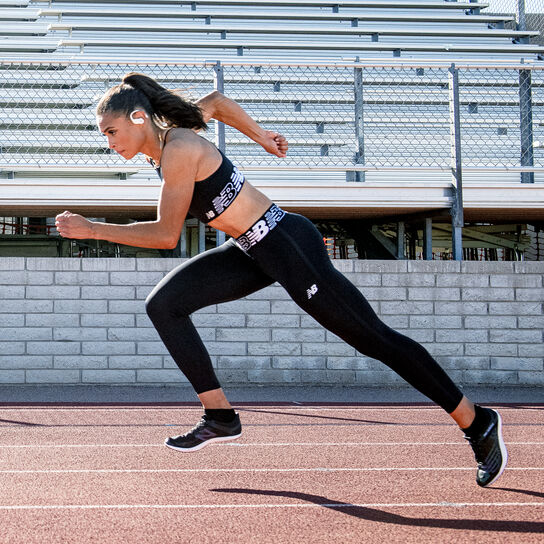 Side profile of Sydney McLaughlin, a female runner, running on a track with bleachers in the background
